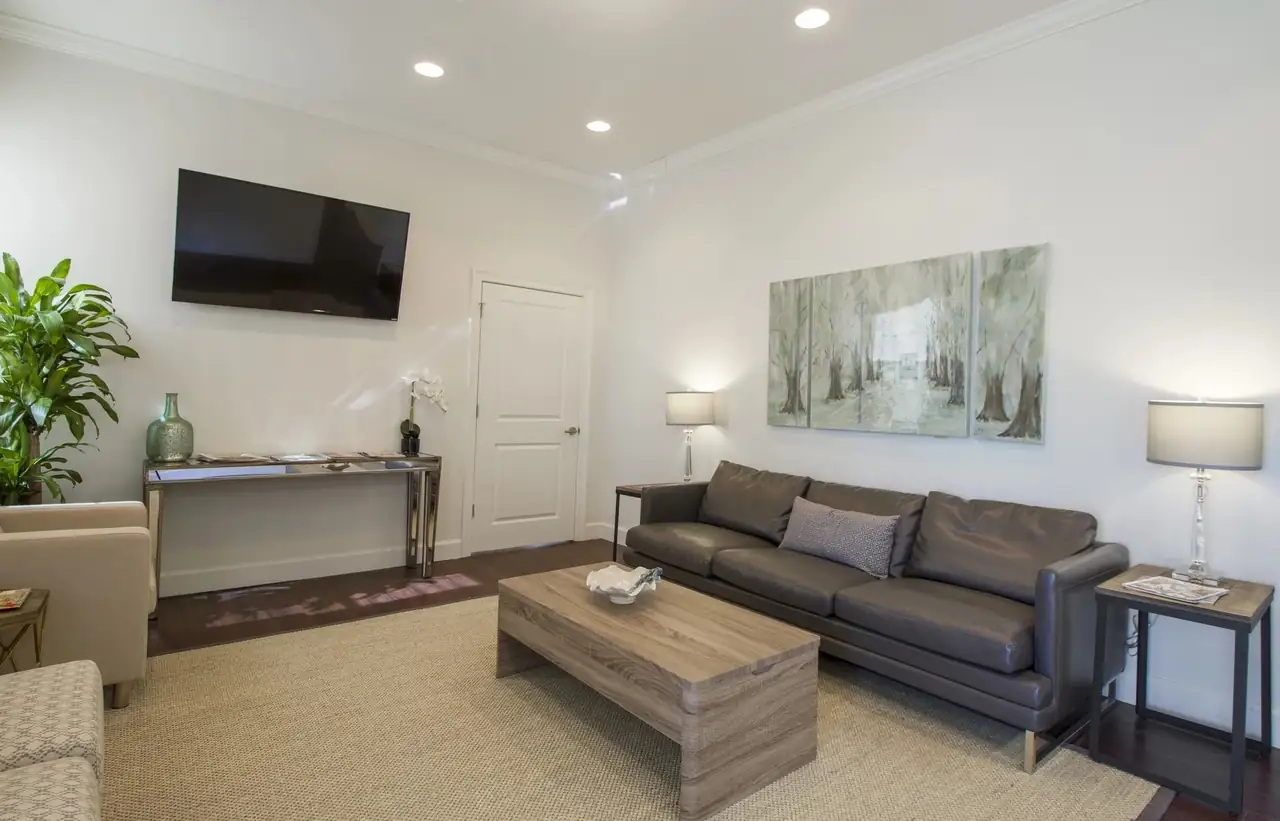 The waiting room at Uptown Dental on St. Charles Avenue: a grey leather sofa, a wooden coffee table and a painting of oak trees.